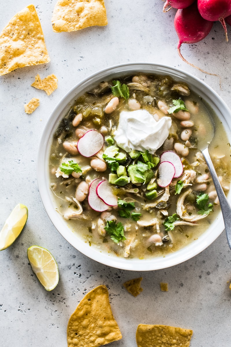 Green Chicken Chili in a white bowl topped with sour cream, cilantro, avocados and sliced radishes.
