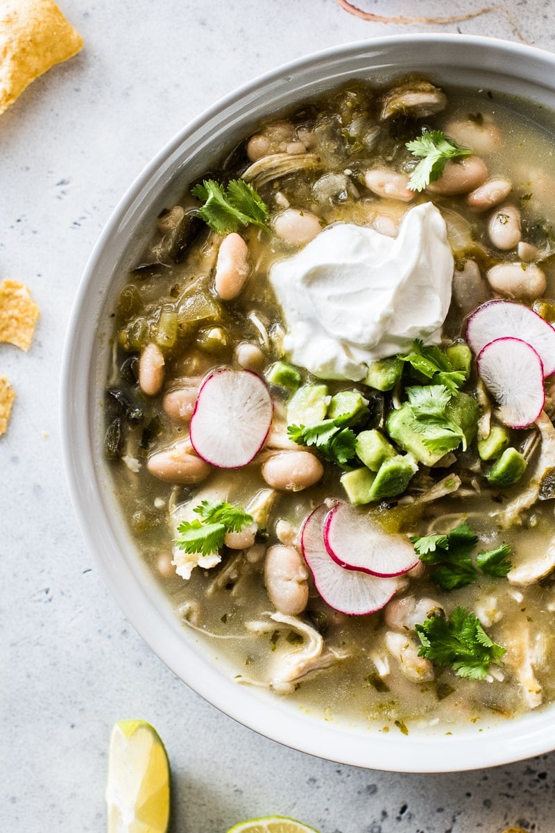 Green chicken chili in a bowl topped with cilantro, radishes, and sour cream.