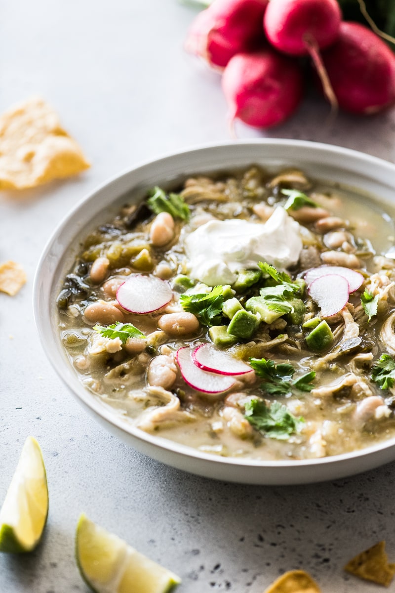 Green Chicken Chili on a table next to tortilla chips and lime wedges.