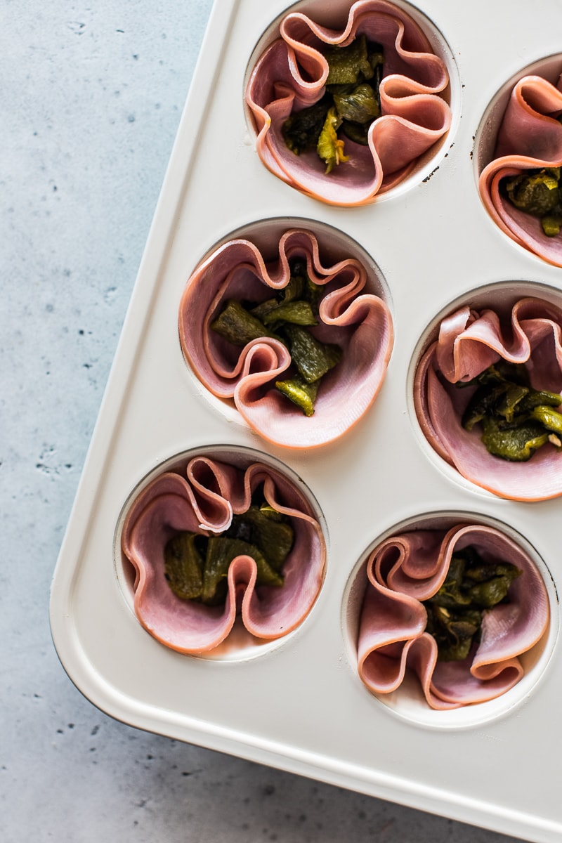 Deli ham slices and chopped roasted poblanos in muffin tin cups.