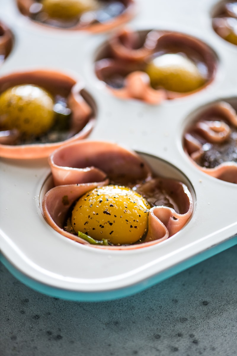 A cracked egg with the yolk in an egg muffin cup topped with black pepper and salt.