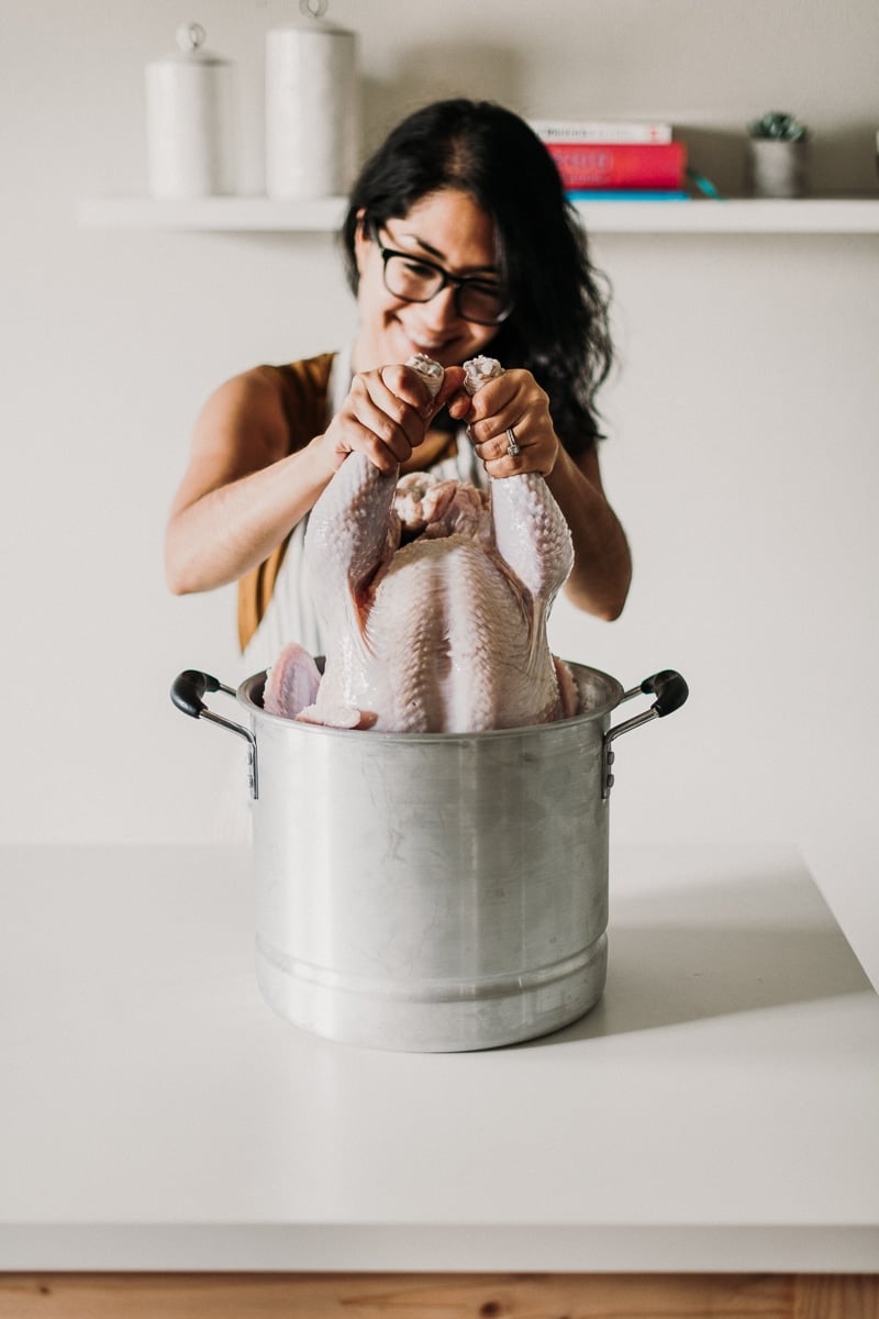 A turkey being lifted out of a stockpot full of brine.