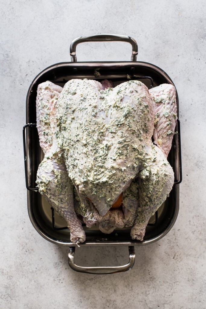 A turkey in a roasting pan covered with herb butter.