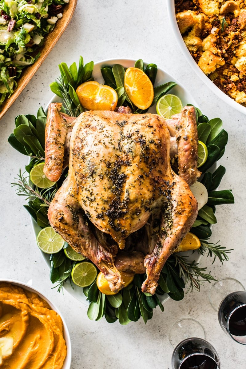 An herb roast turkey on a large platter next to Thanksgiving side dishes.