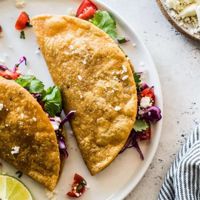 Potato tacos on a white plate stuffed with shredded cabbage and pico de gallo.