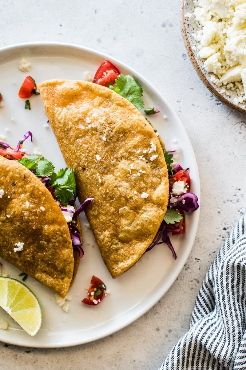 Crispy Potato Tacos on a white plate stuffed with shredded cabbage and pico de gallo.