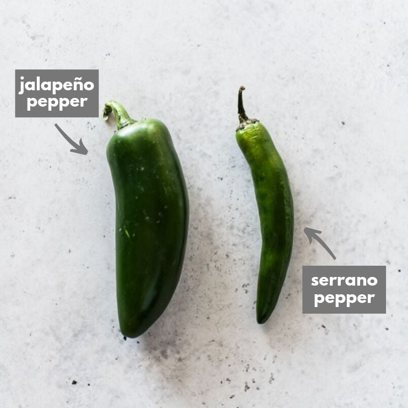 A serrano pepper next to a jalapeno pepper.