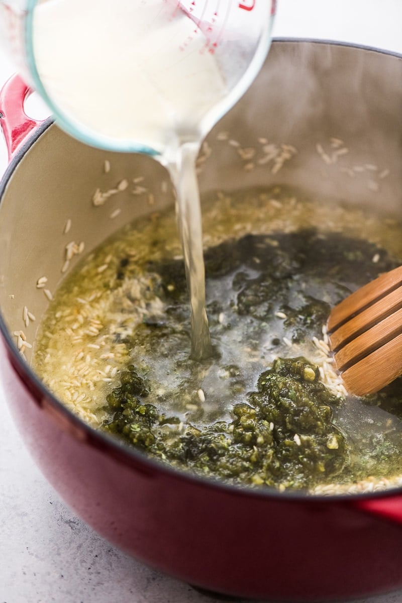 Chicken broth being poured into a dutch oven for arroz verde (green rice).