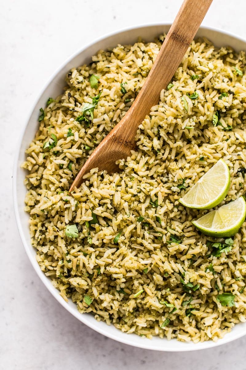 A bowl of arroz verde topped with cilantro and lime wedges.
