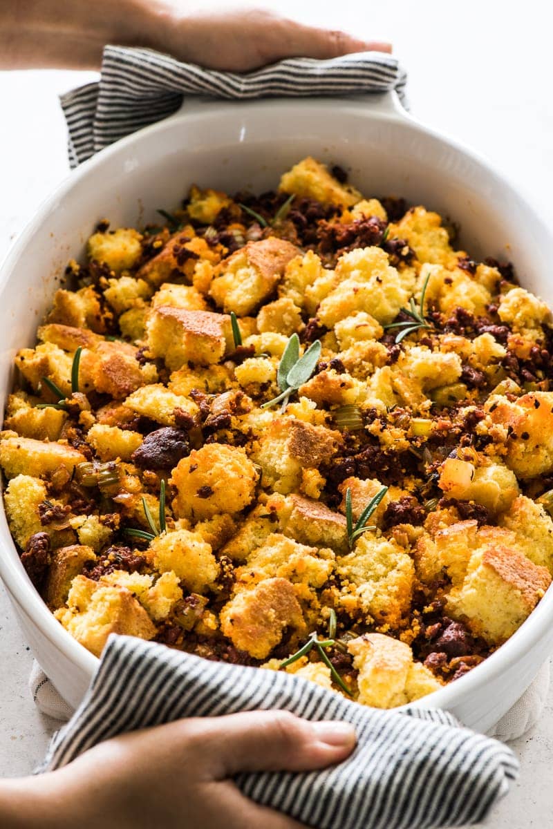 Cornbread stuffing in a baking dish topped with fresh sage and rosemary.