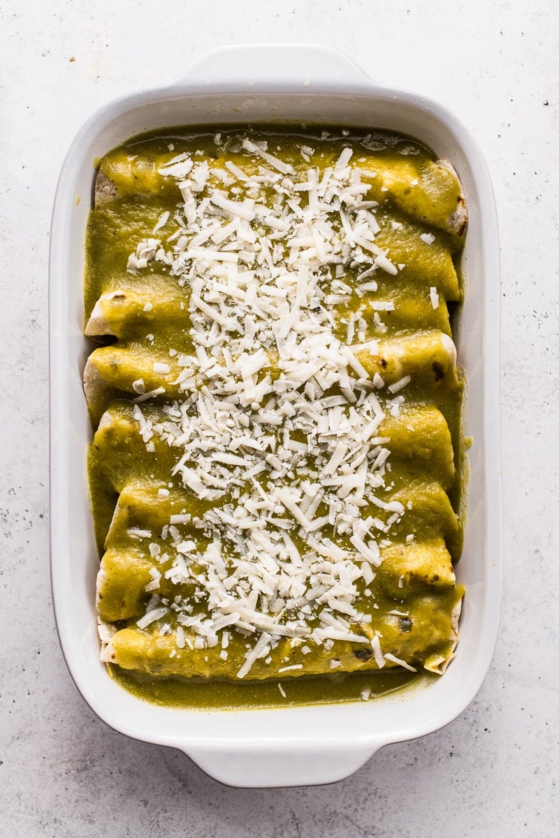 A casserole of chicken enchiladas topped with green enchilada sauce.