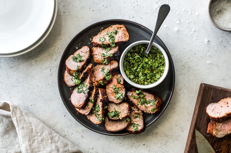 Grilled pork tenderloin slices on a plate topped with a green herb sauce.