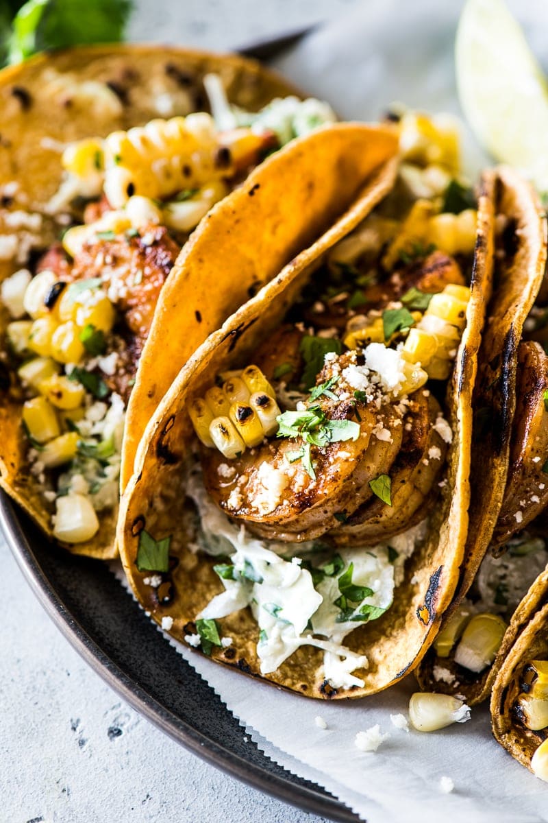 Grilled shrimp tacos on a plate topped with cotija cheese, cilantro and grilled corn.