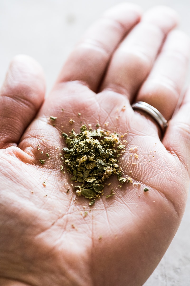 The palm of a hand holding Mexican oregano that has been rubbed and broken 