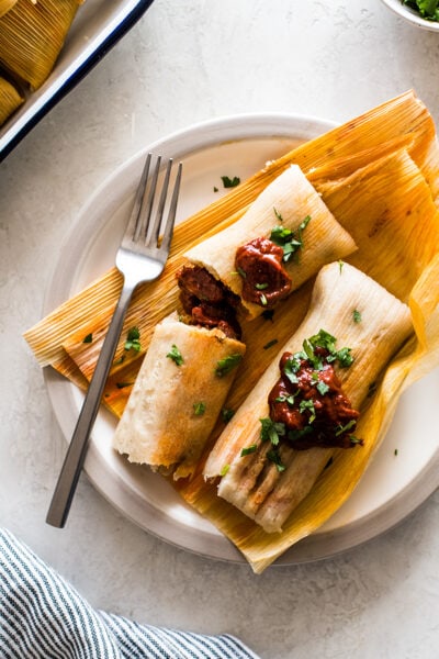 Pork Tamales with red chile sauce on corn husks.