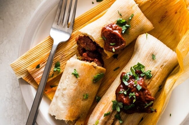Pork Tamales with red chile sauce on corn husks.