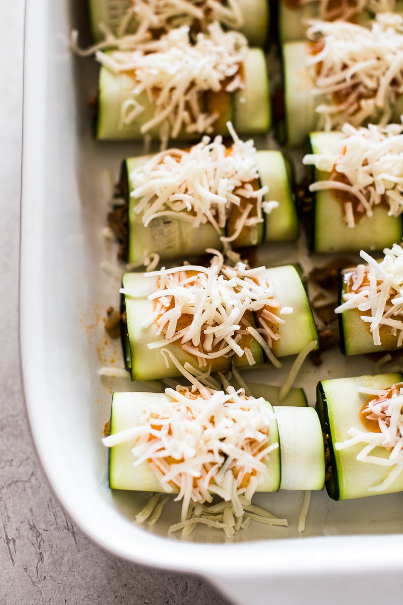 Rolled zucchini enchiladas topped with sauce and shredded cheese