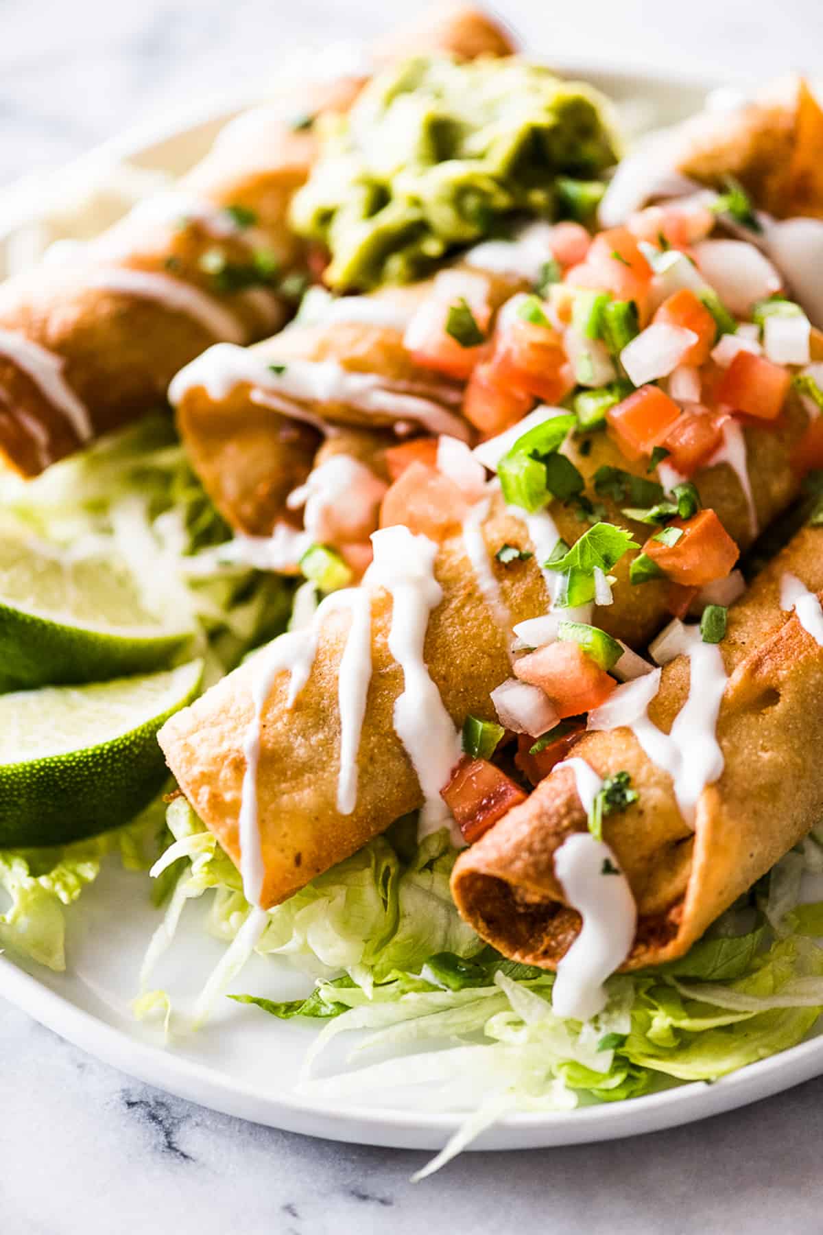 Crispy chicken taquitos on a plate with Mexican crema, shredded lettuce, and pico de gallo.