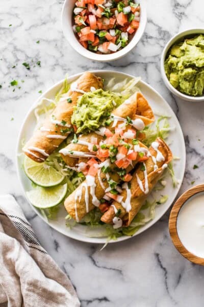 Chicken taquitos on a plate with shredded lettuce and pico de gallo.