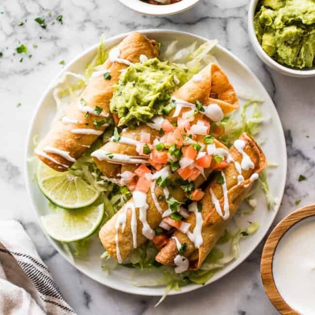 Taquitos de poulet sur une assiette avec de la laitue râpée et du pico de gallo.