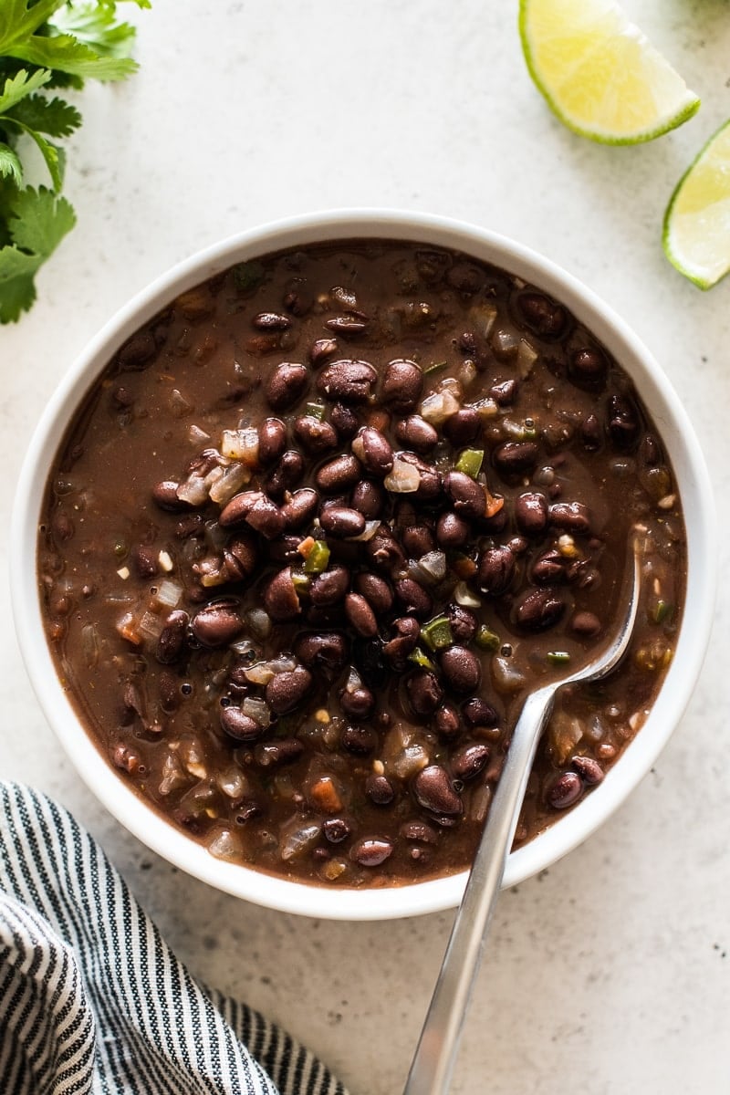 A bowl of cooked and seasoned black beans with a spoon dipped in it