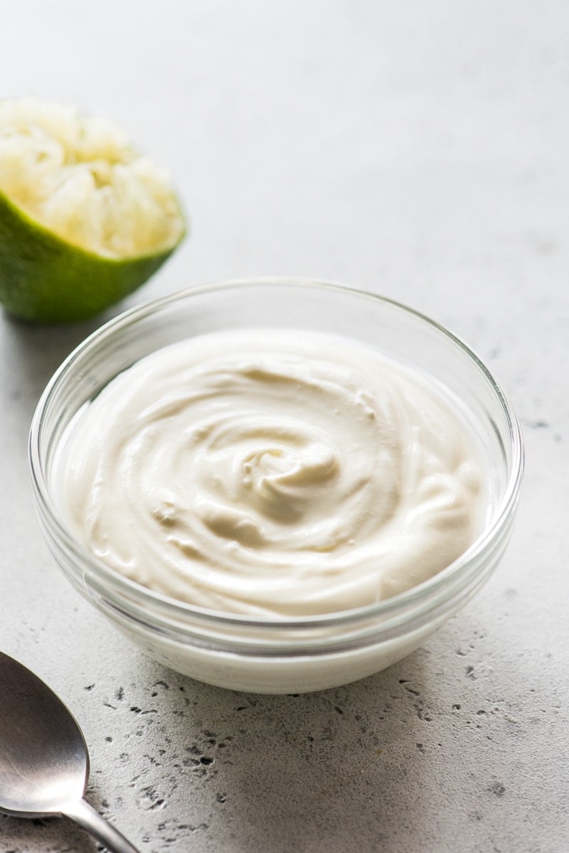 Homemade Mexican Crema in a clear glass bowl next to a lime wedge.