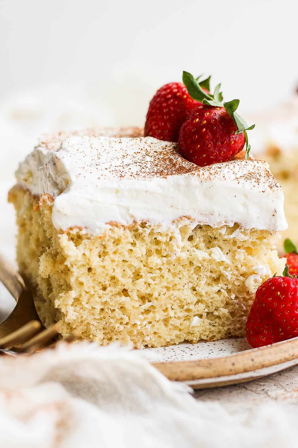 A slice of tres leches cake on a plate topped with whipped cream and fresh strawberries.