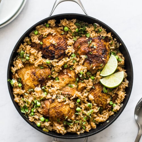 Arroz con pollo in a pan topped with cilantro and lime wedges.