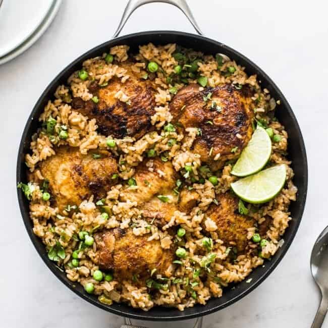 Arroz con pollo in a pan topped with cilantro and lime wedges.