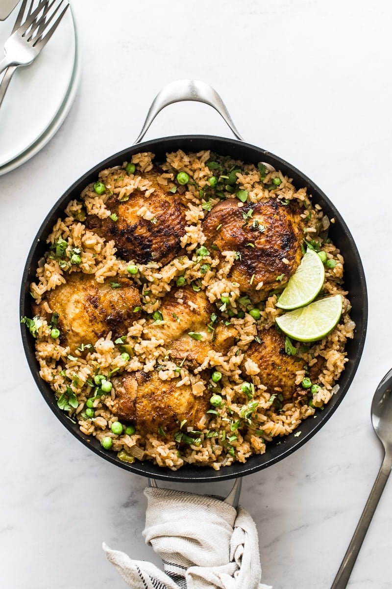 Arroz con pollo in a pan topped with cilantro and lime wedges.