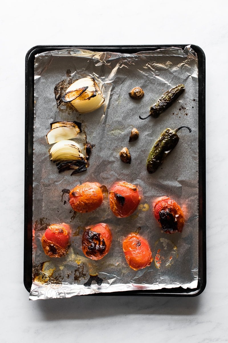Roasted tomatoes, onions, jalapenos and garlic on a baking sheet.