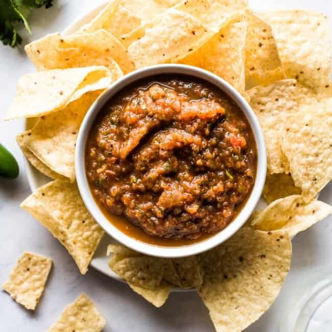 Roasted tomato salsa in a bowl surrounded by tortilla chips.