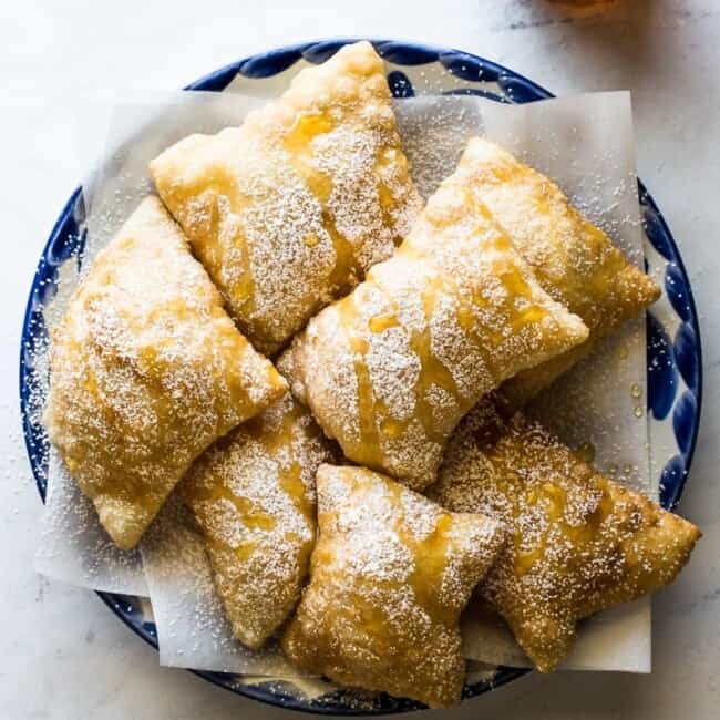 Sopapillas topped with powdered sugar and honey on a plate.