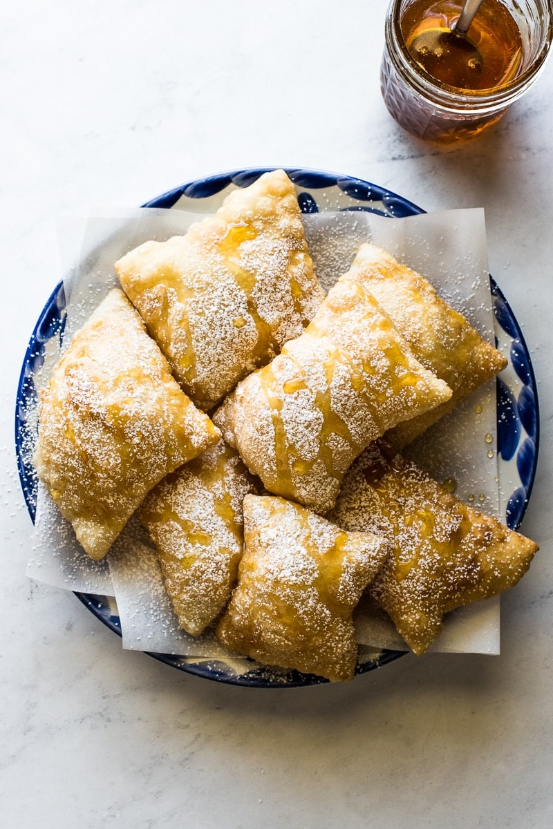 Sopapillas topped with powdered sugar and honey on a plate.