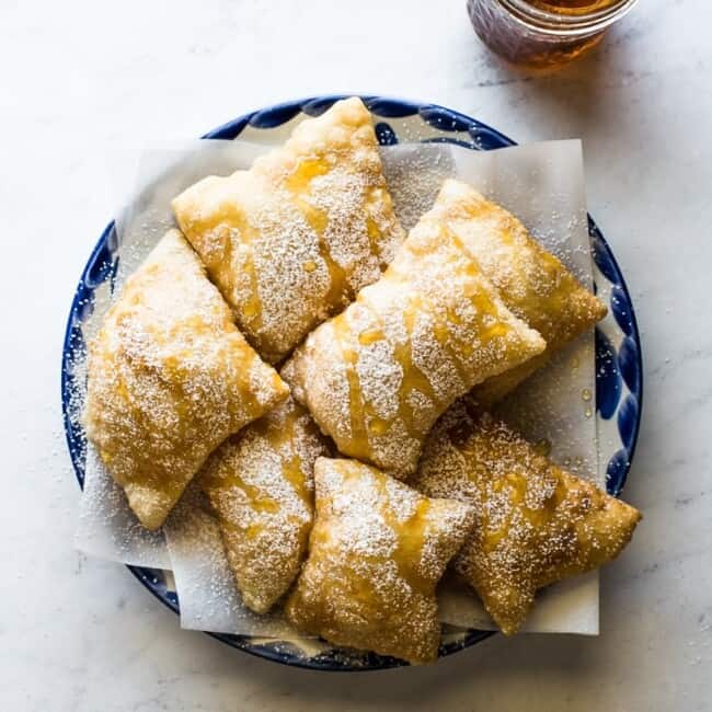 Sopapillas topped with powdered sugar and honey on a plate.