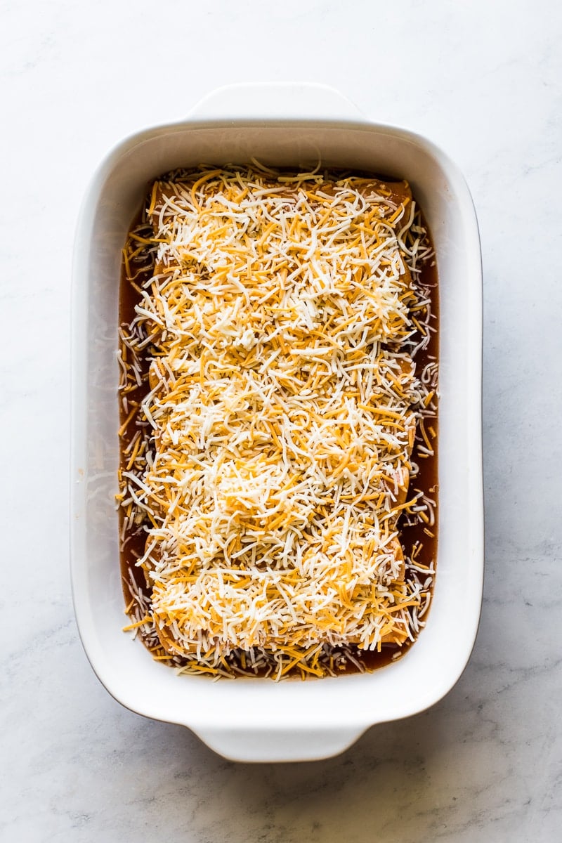 Chicken enchiladas topped with shredded cheese ready to be baked.