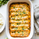Chicken enchiladas in a baking dish topped with cilantro.