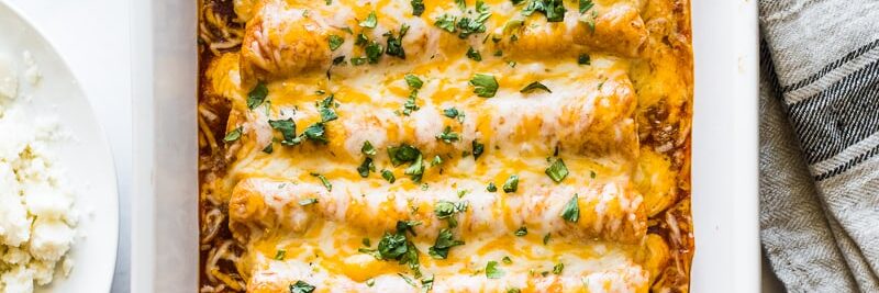 Chicken enchiladas in a baking dish topped with cilantro.