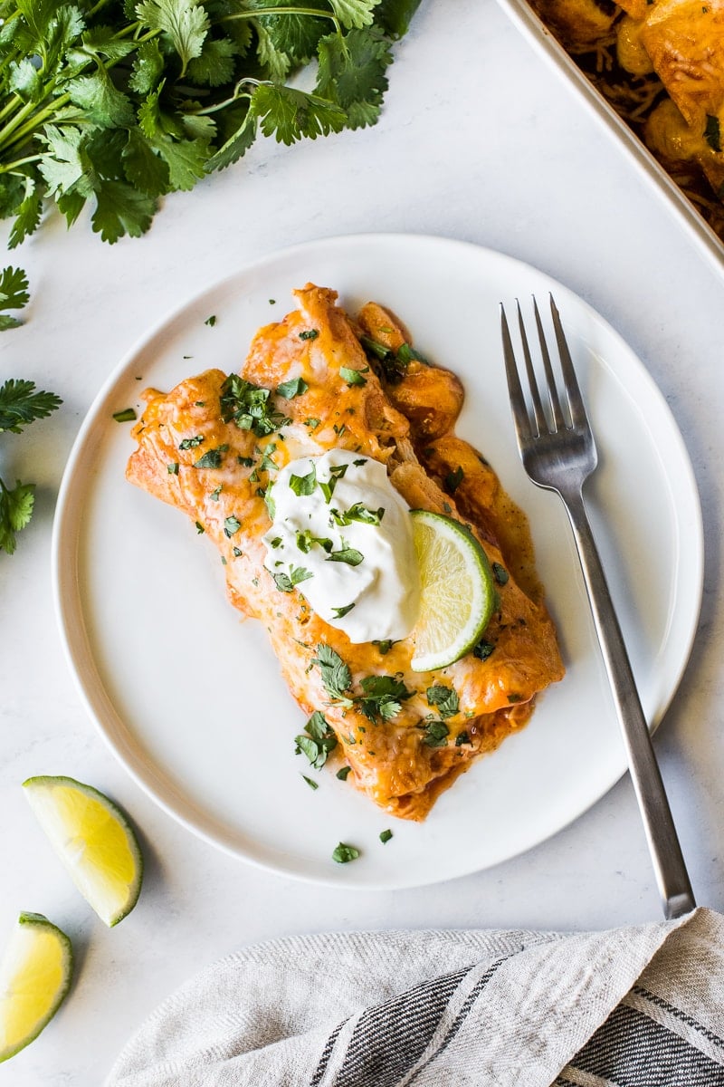 Chicken enchiladas on a plate topped with sour cream.