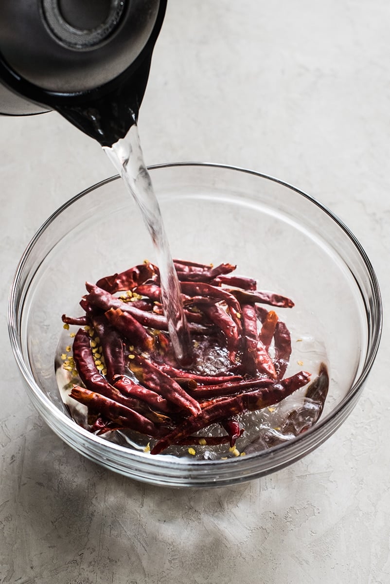 Dried chile de arbol peppers in a bowl being rehydrated with hot water.