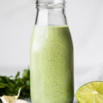 Cilantro Lime Dressing in a jar next to fresh limes and garlic cloves.