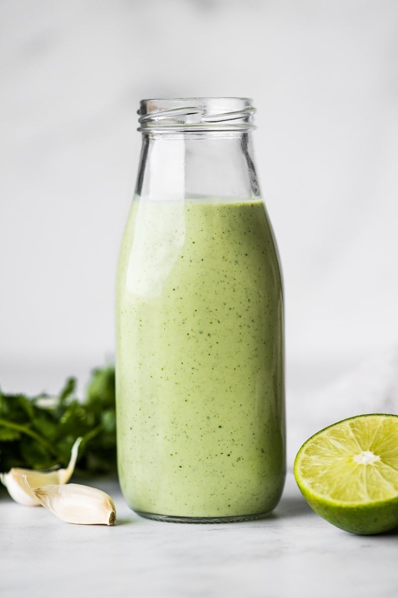 Cilantro Lime Dressing in a jar next to fresh limes and garlic cloves.