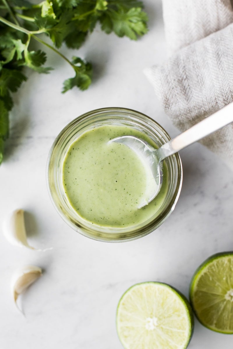 Cilantro lime dressing in a glass jar with a spoon in it.