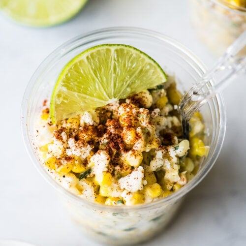 Esquites in a cup topped with chili powder and a lime wedge.