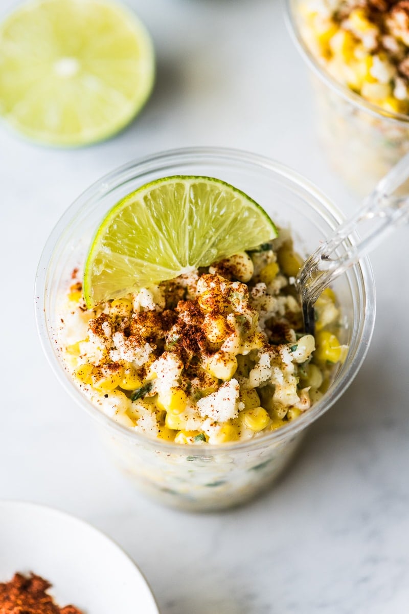 Esquites in a cup topped with chili powder and a lime wedge.