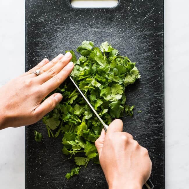 Two hands chopping cilantro on a cutting board.