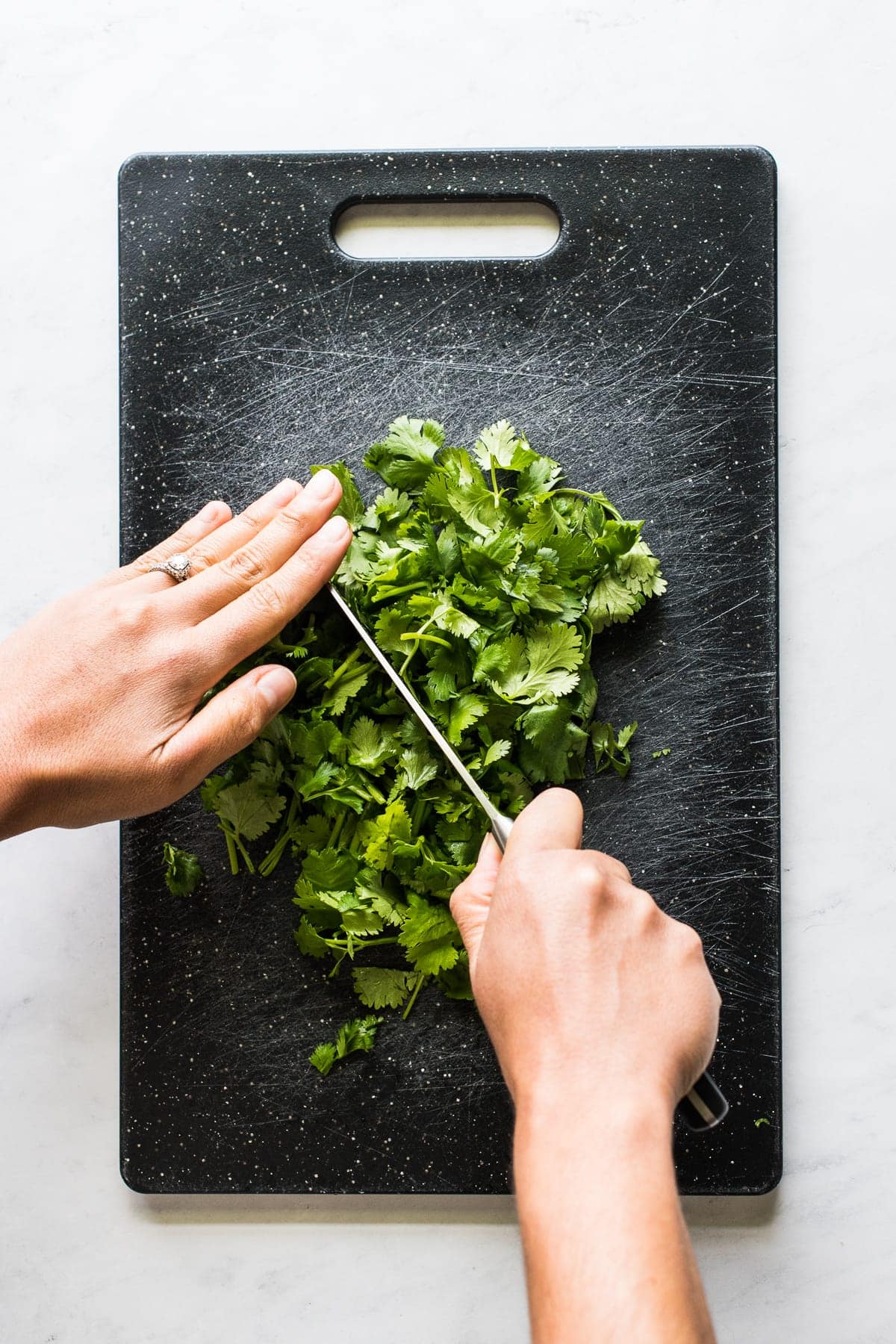 Two hands chopping cilantro on a cutting board.