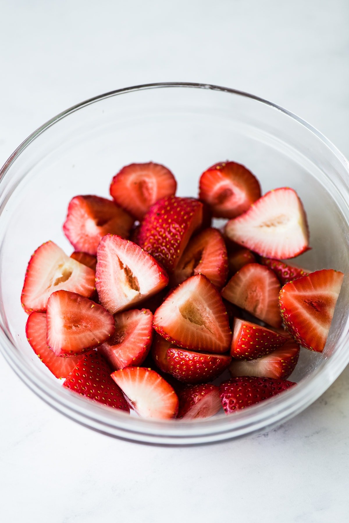 Fresh cut strawberries in a clear class bowl.