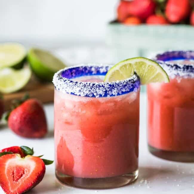 A strawberry margarita in a glass garnished with a lime.