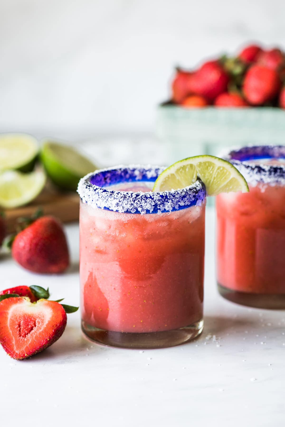 A strawberry margarita in a glass garnished with a lime.